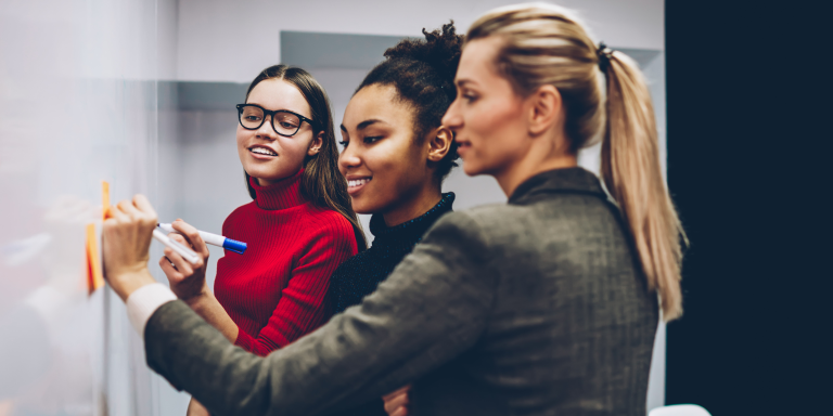 Three adults writing on a dry-erase board during a coaching session.